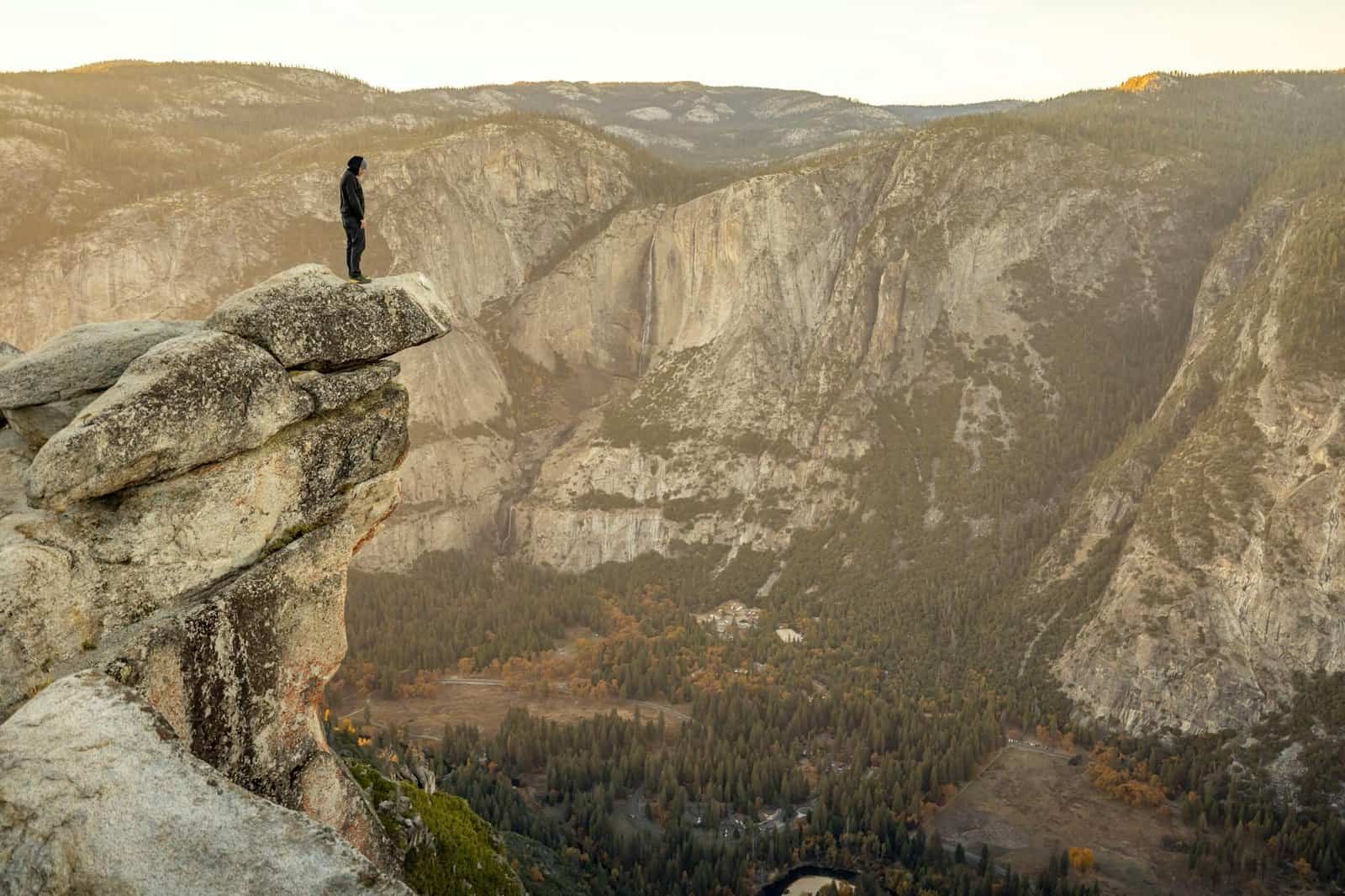 A lone adventurer stands on a cliff edge overlooking Yosemite Valley at sunset